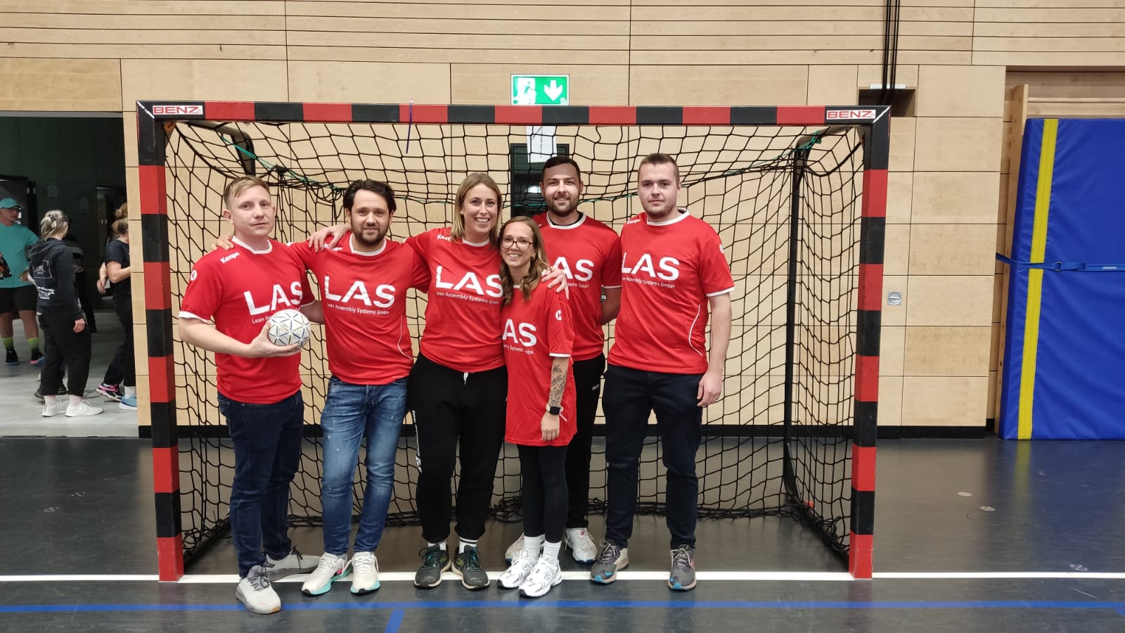 Six employés de LAS en maillot d'entreprise se tiennent devant un but de handball