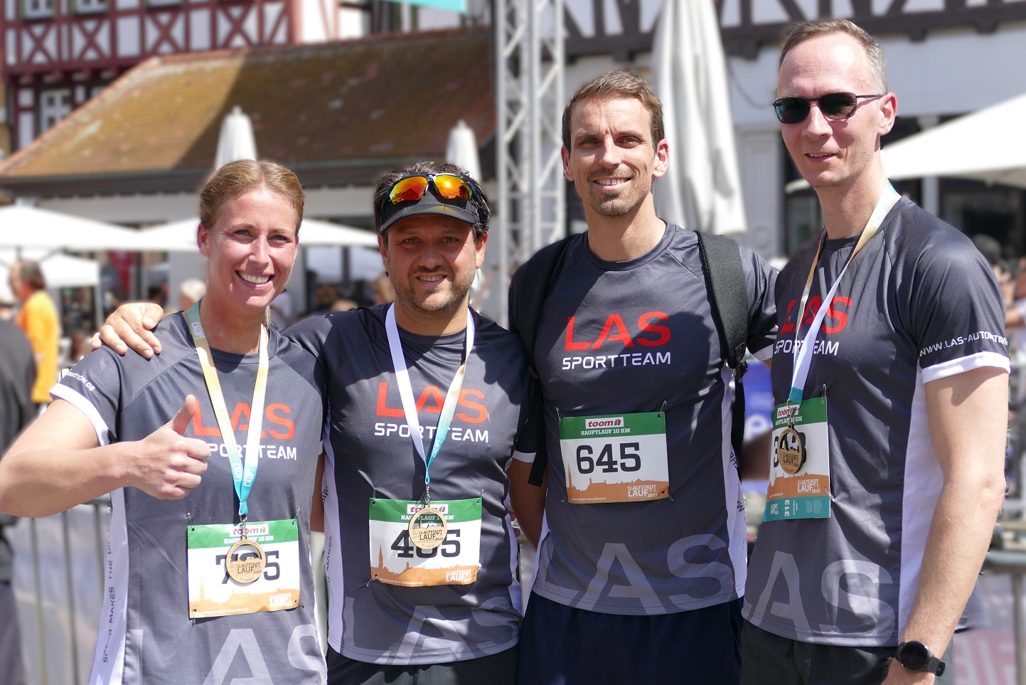 Schorndorfer Altstadtlauf 2025 Die vier Läufer des LAS-Teams stehen mit Medaillen um den Hals vor dem Zielportal
